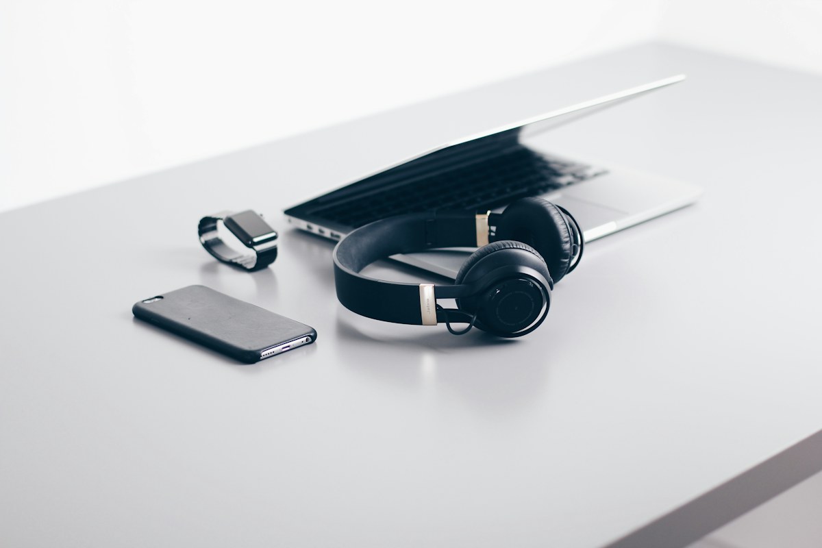 Laptop, headphones, phone and smartwatch on a light studio surface